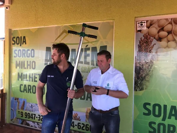 Atendimento no escritório, com o banner de soja, sorgo, milho e milheto ao fundo